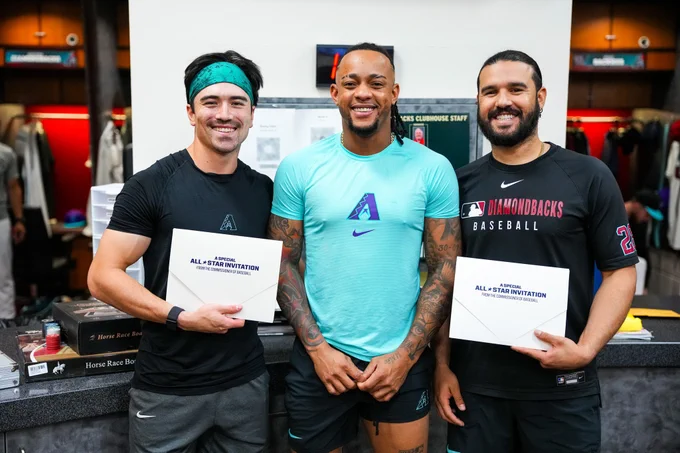 Corbin Carroll, Ketel Marte, and Eugenio Suárez pose for a photo. Carroll and Suárez are holding envelopes that say, "A special All-Star invitation from the Commissioner of Baseball" on it. 
