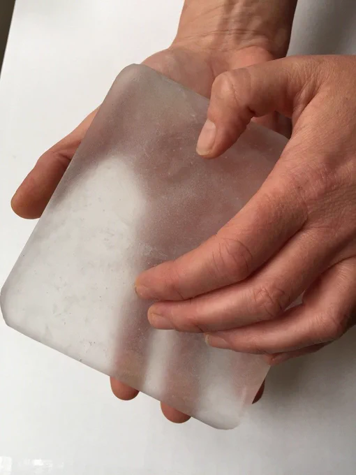 A pair of hands holds a large square ice block.