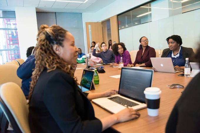 Several people sat around laptops participating in a boardroom meeting.