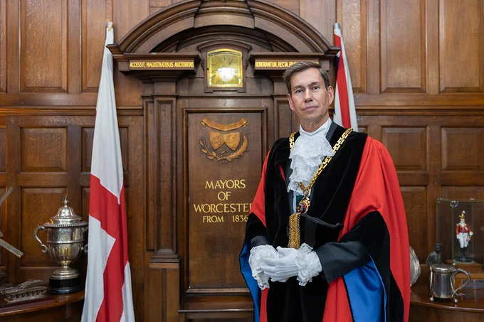 The Mayor of Worcester standing in front of elaborate wooden panelling inside the Guildhall