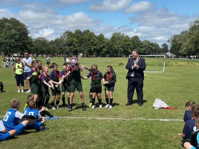 Mayor of St Helens borough, Cllr Seve Gomez-Aspron, pictured clapping alongside a group of children wearing medals and raising a plaque at football presentation in Sutton Park