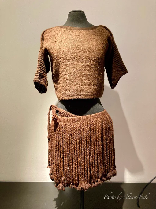 My photo shows a short-sleeved brown woollen tunic top and a brown woollen skirt made of cords which hang down from a narrow woven band like a fringe. It is a copy of the costume worn by so-called ‘Egtved Girl’, a 16-18 year old young woman whose well-preserved oak-coffin grave, dated 1370 BC, was excavated in 1921. The original skirt was wrapped twice around the girl’s waist and measures 38 cm in length. On display at the National Museum of Denmark in Copenhagen