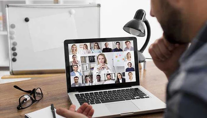 Man attending a virtual video conference on a laptop with multiple participants displayed on screen, indicating a remote team meeting or online collaboration setup.