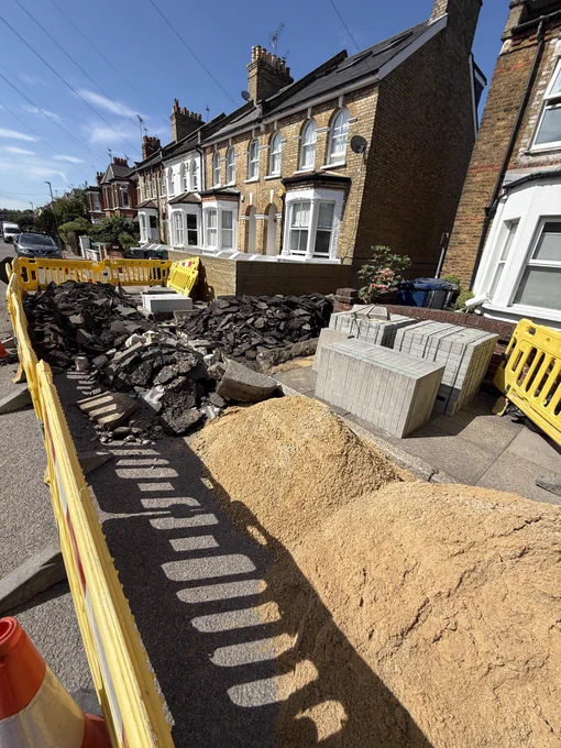 A dug-up tarmac path surrounded by yellow construction barriers.