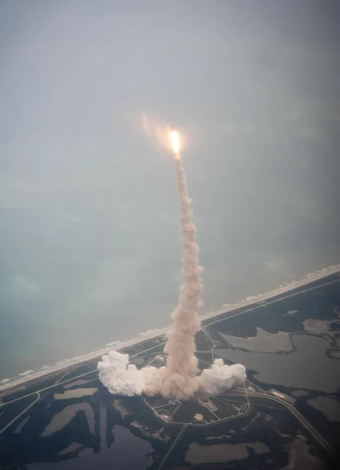 A trail of exhaust from the launch pad to space shuttle Atlantis is seen through the window of a Shuttle Training Aircraft (STA) as it launches from Kennedy Space Center on the STS-135 mission, Friday, July 8, 2011.  Photo Credit: (NASA/Dick Clark)