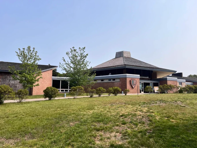 Green grass leads up to a brick and shingled visitor center building.