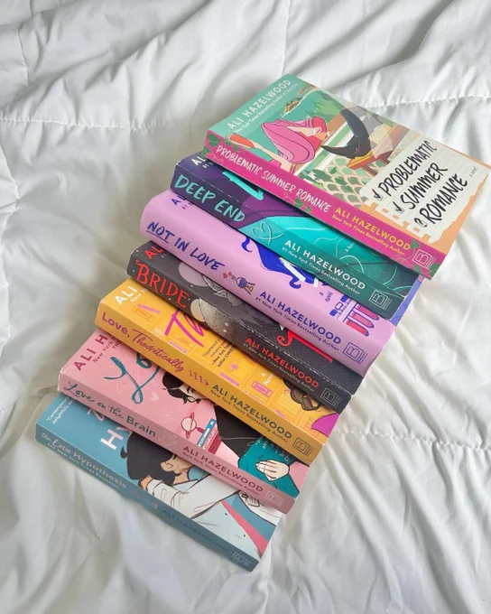 An array of physical copies of Ali Hazelwood's books which includes: "The Love Hypothesis", "Love on the Brain", Love, Theoretically", "Bride", "Not in Love", "Deep End", and "Problematic Summer Romance"