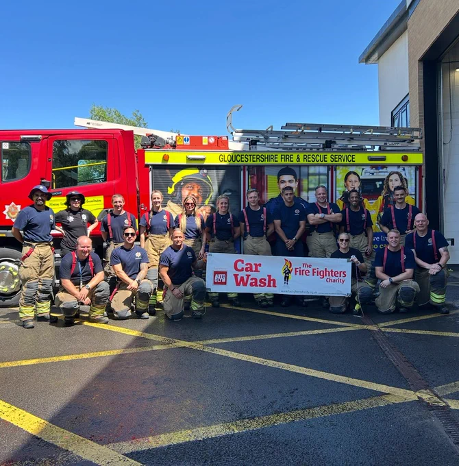 Fire fighters stood in front of a fire engine holding a car wash sign.