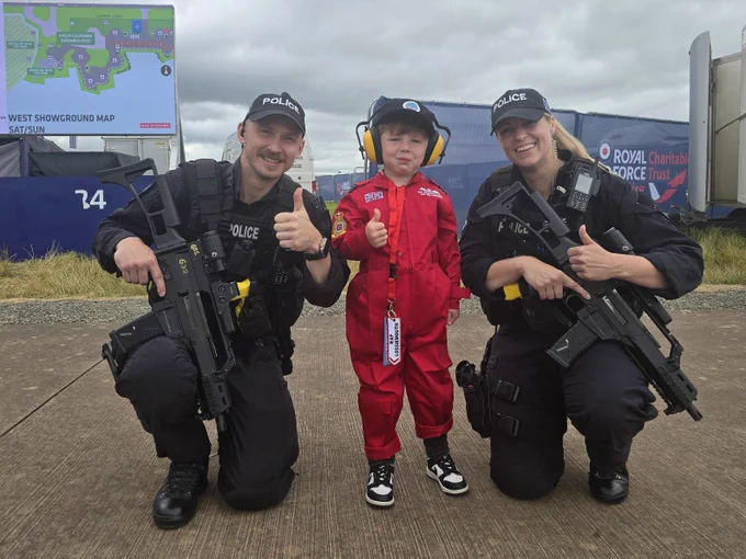 Two armed officers kneeling alongside a child at the Royal International Air Tattoo in 2024