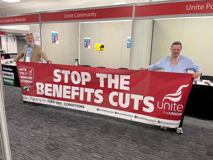 Activists hold a read and white banner with logos of unite for a workers economy and unite.  In white text it says stop the benefits cuts