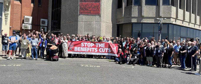 Delegates from unite policy conference stand outside Brighton conference surrounding a red banner with white text that says stop the benefits cuts