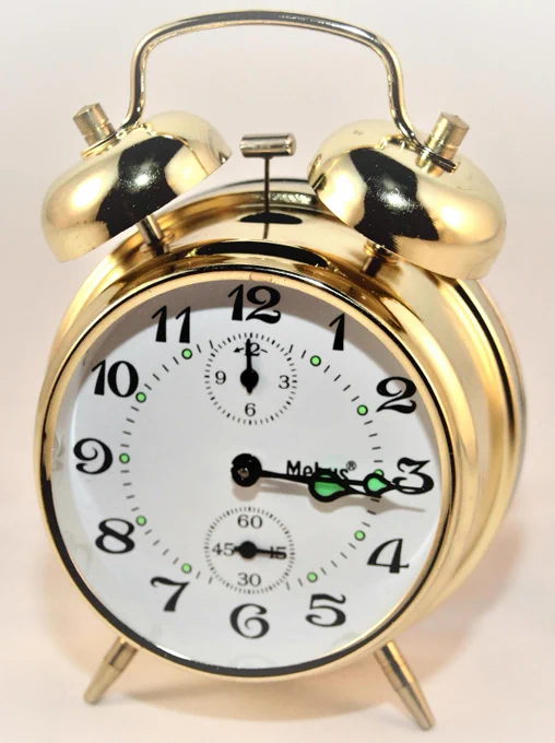 A classic brass alarm clock featuring twin bells and a white face with black numbers.