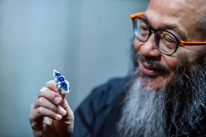Photograph of a man wearing orange and black glasses and looking at a piece of blue porcelain. Photo courtesy of Wallace Chan.