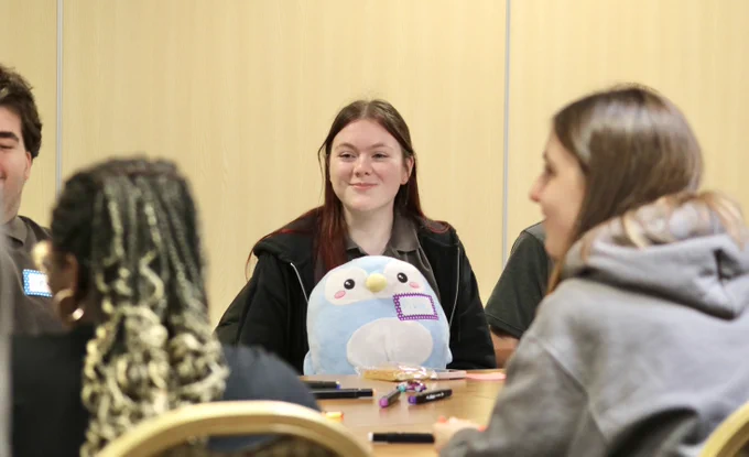a young girl smiling at a table with a plush penguin