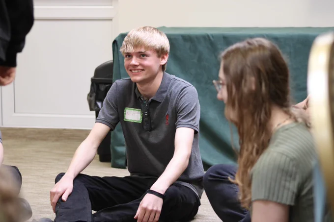 a young man sat on the floor smiling up at someone