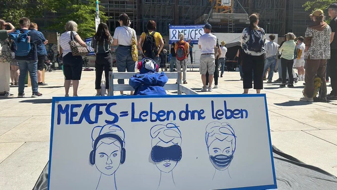 Ein Plakat mit dem Slogan „ME CFS = Leben dürfen leben" zeigt verschiedene Darstellungen von Personen mit medizinischen Hilfsmitteln und ist Teil einer Demonstration.