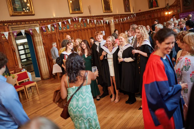 Colour photo of School of Divinity graduating students stood smiling together in the Rainy Hall as they prepare to take a photo.