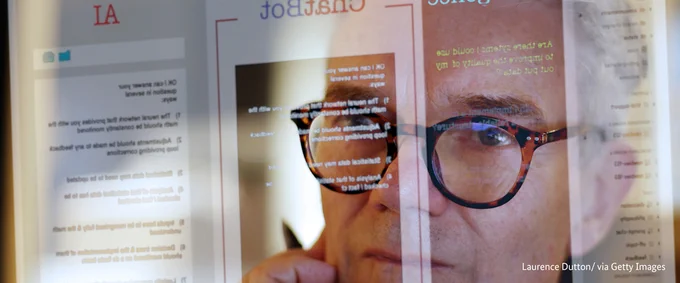Ein Mann mit Brille blickt konzentriert aufeinen Bildschirm. Auf dem Bildschrim sind die Wörter AI und Chatbot zu erkennen.