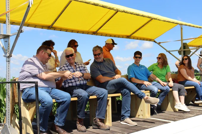 A group of field day attendees sitting beneath a canopy and talking with one another.