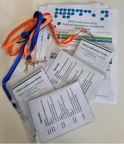 A pile of conference programmes and lanyards sit on a table awaiting collection by conference attendees