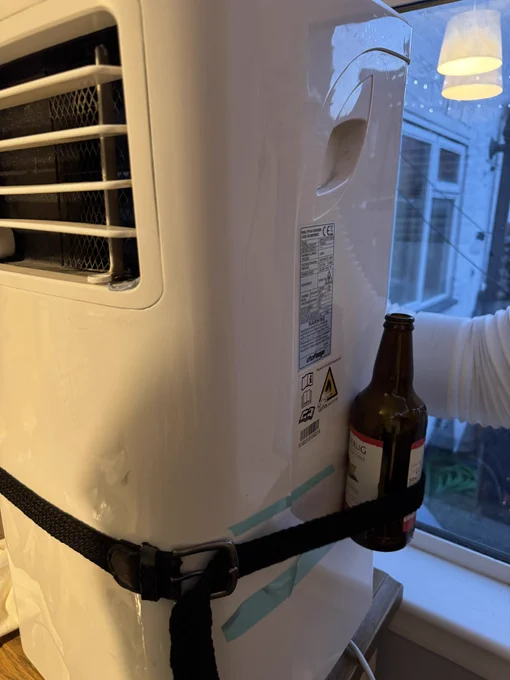 A portable air conditioner with an empty bottle of rekorderlig cider strapped onto the side of it with an elasticated belt.