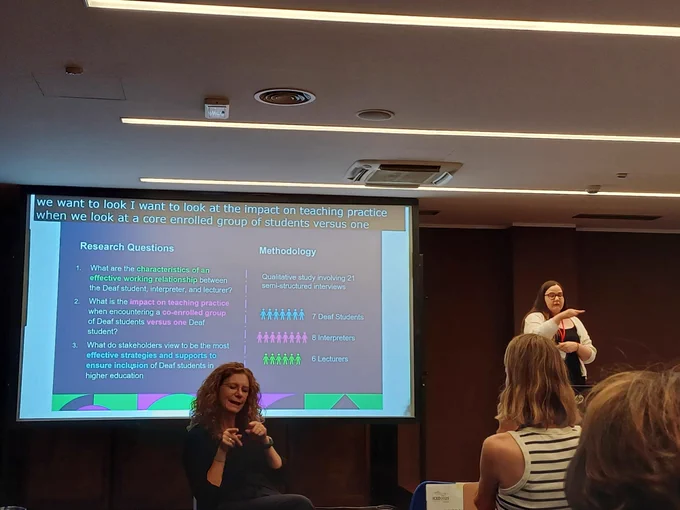Caroline presenting on stage. Accompanied by slides with her research questions and methodology. 
