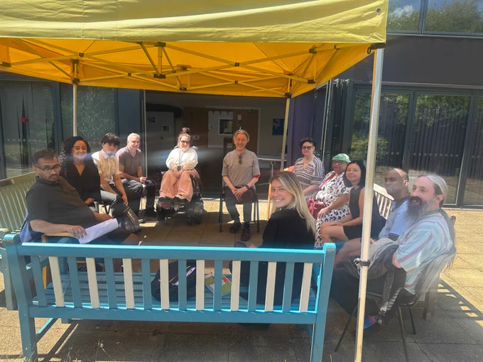  A group of 12 people positioned in a semi circle under a yellow gazebo. 