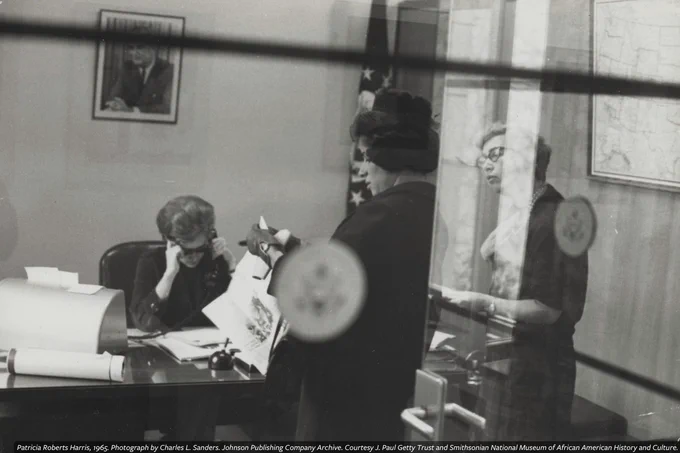 A black-and-white photograph of Patricia Roberts Harris and two colleagues working in an office, photographed by Charles. L. Sanders, 1965.