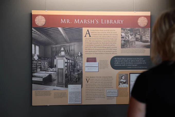 A woman is looking at an exhibit panel on a wall titled "Mr. Marsh's Library."