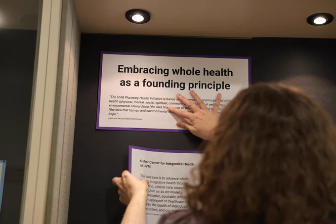 A woman is pasting an exhibit panel titled "Embracing whole health as a founding principle" into an exhibit case. 
