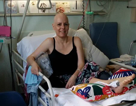 A patient in a hospital bed after receiving surgery for primary bone cancer in her foot. Her leg is elevated and resting on a pillow. 