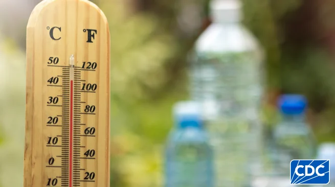 Outdoor thermometer showing temperature over 100 degrees. Water bottles shown blurred in background. 