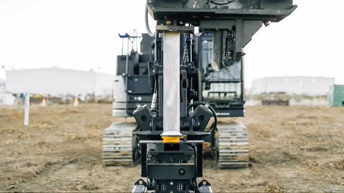 Close-up view of autonomous robots working together to drive a metal beam at a construction site.