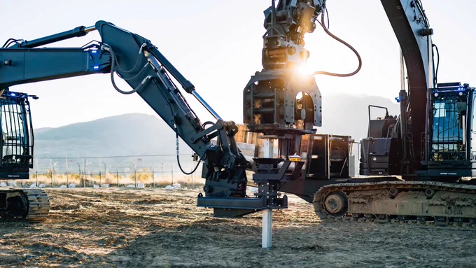Two robots equipped with drilling attachments operating in a field at sunset.