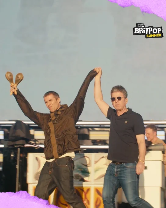 Liam and Noel walking on stage holding hands, raised high between them