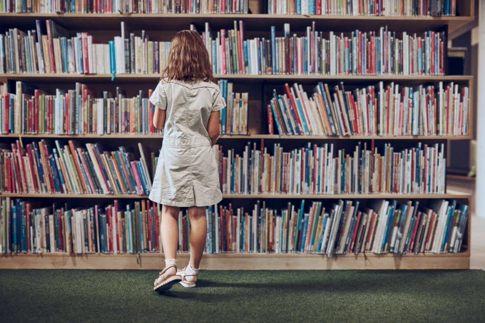Photo of a young girl standing in front of a full library bookshelf.