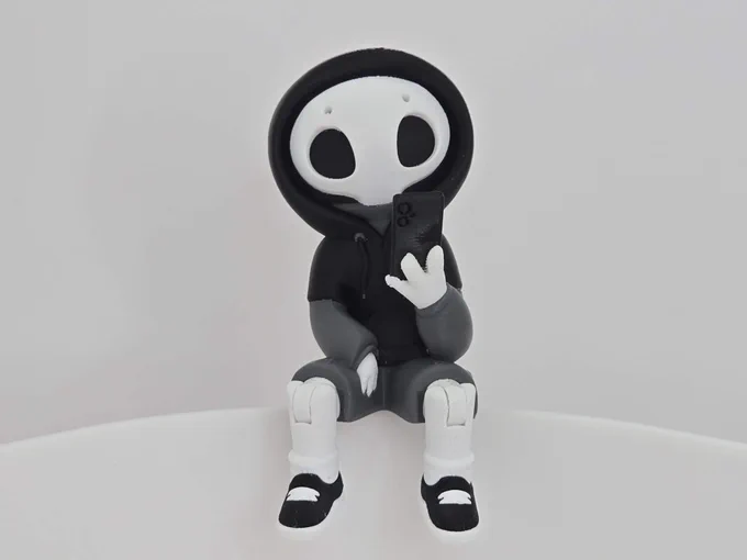 Front view of Project Hazy sitting with legs bent, wearing a black hoodie and holding a smartphone. Printed in black, gray, and white PLA.