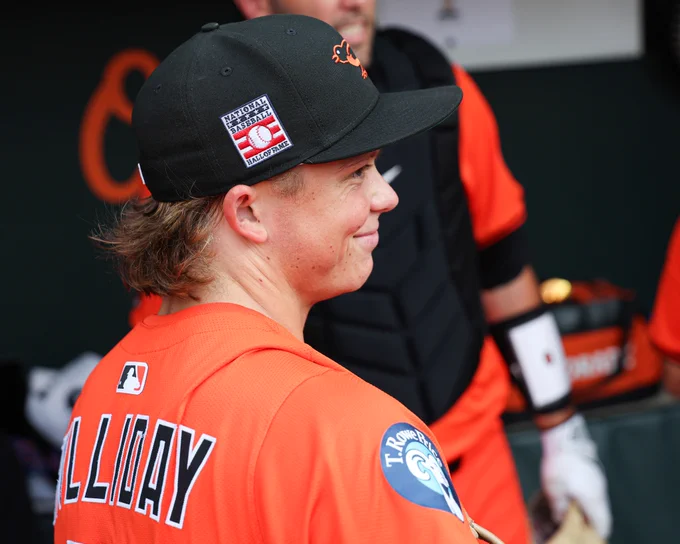Jackson Holliday in the Orioles dugout before tonight's game. He is wearing an all orange Orioles uniform and Hall of Fame Weekend Orioles cap.