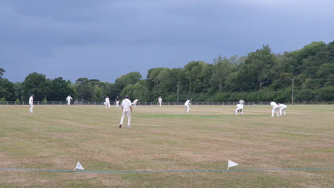 View from boundary shows slip, gully and other fielders watching on as batter tries to hit ball as umpire looks on