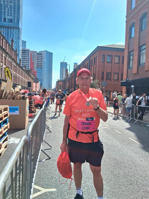 Participant in a pink outfit running in the Great Manchester Run, with spectators and buildings in the background.