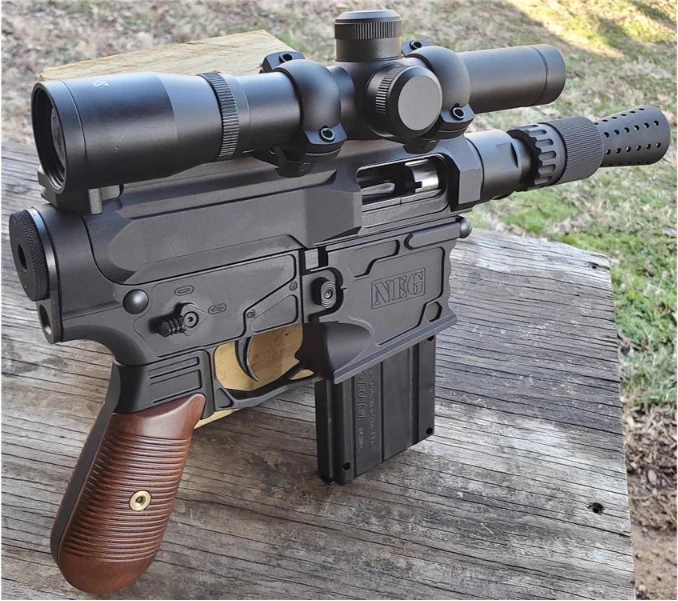 Close-up view of a firearm with a wooden grip and mounted scope, positioned upright on a wooden surface outdoors.