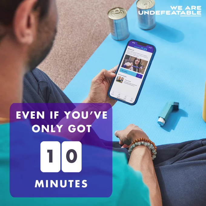 Man sitting on yoga mat with tin cans and inhaler on the mat, he's using a fitness app on a smartphone, with text that reads, 'Even if you've only got 10 minutes.' 