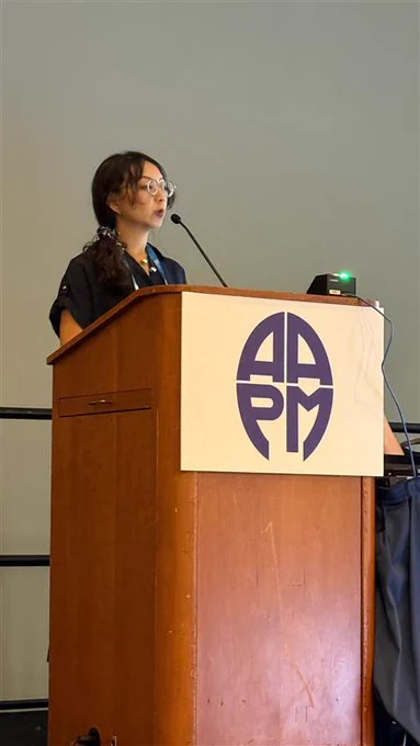 A woman standing behind an AAPM podium and giving a talk.