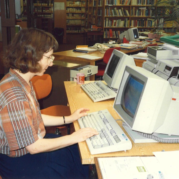Image of the Library from the 1970s with a Librarian in the foreground working at her desk.