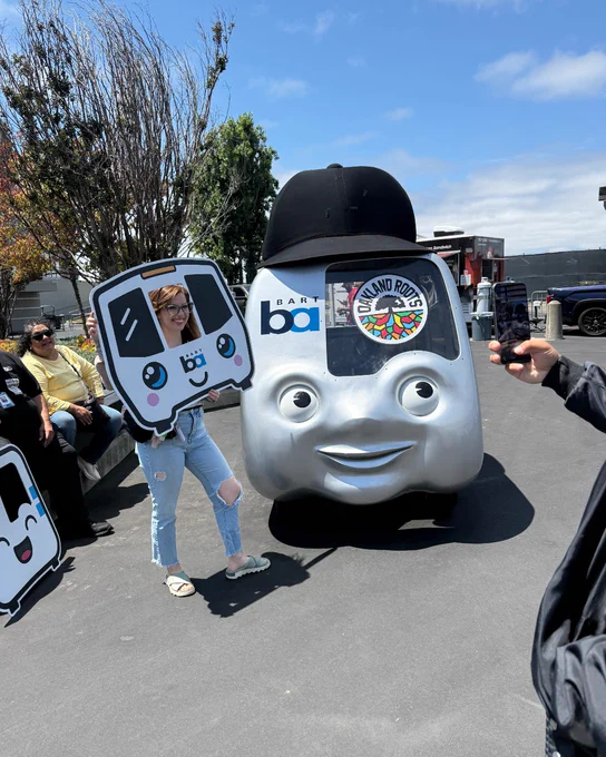 a woman poses in front of the BARTmobile with a BART selfies cut out