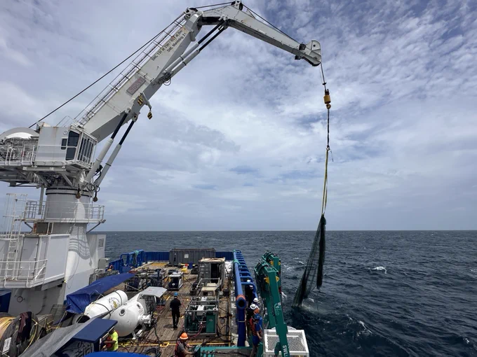 a large crane hauls a large fishing net out of the ocean onto the deck of a research vessel