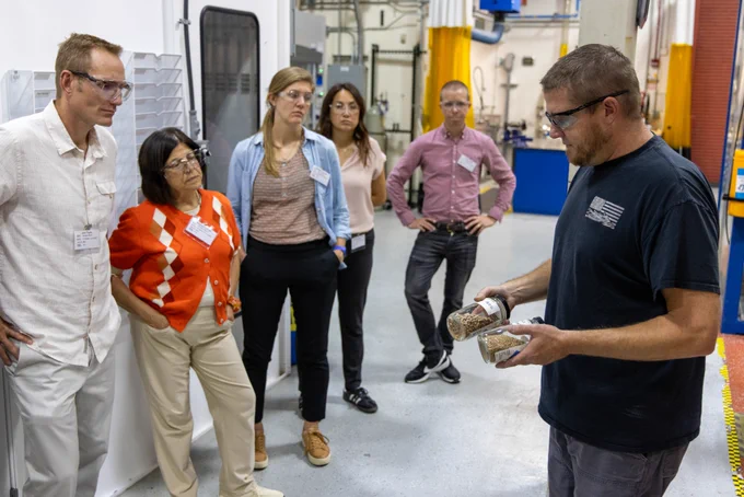 Five people watch a demonstration by a researcher in a lab. 