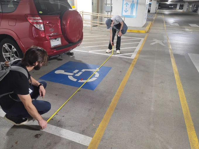 Two people measuring the width of a handicap parking spot. 
