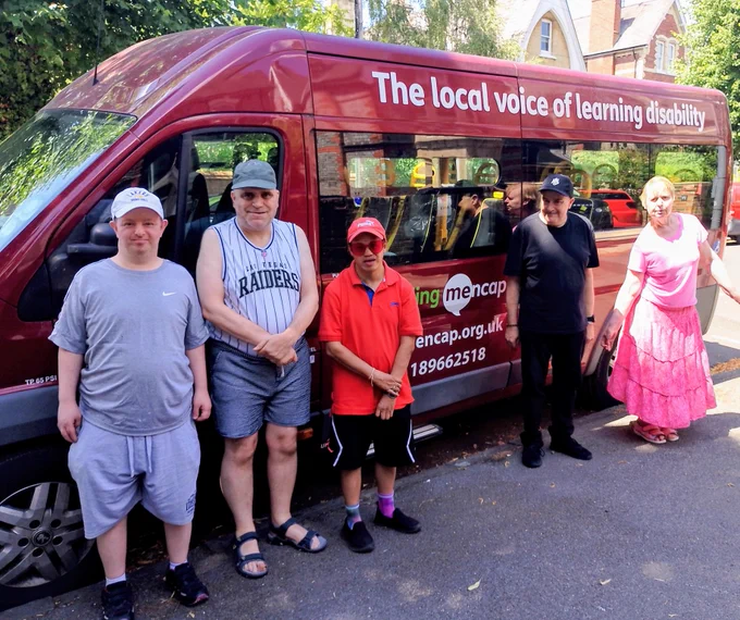 Four men and a woman are standing in front of the red Reading Mencap minibus, which has 'The local voice of learning disability' written on it.