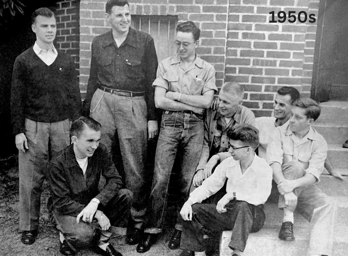 Group of eight young men smiling and posing outside a brick building with '1950s' written on the top right.